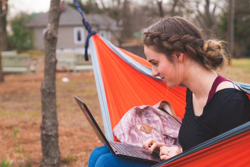 Student sitting in hammock working on laptop