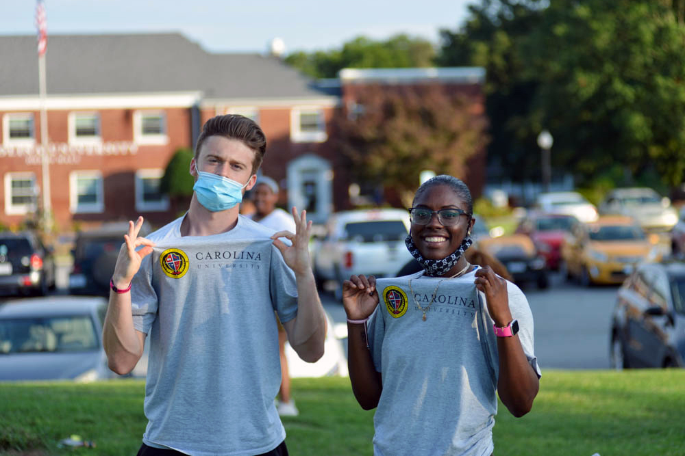 Two students standing in field with Carolina University t-shirts