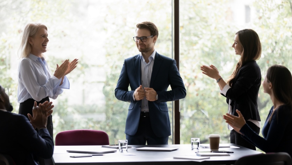 Man standing up at business meeting with people applauding