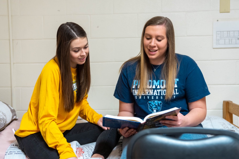 Two female college students looking at textbook in dorm room